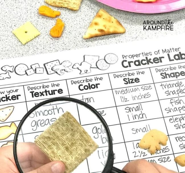 Cracker Properties Science Activities Child's hand holding magnifying glass over a cracker, with worksheet labeled Cracker Lab in the background