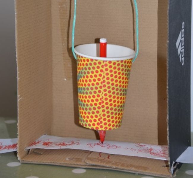 4th Grade Science Science Sparks Paper cup suspended by strings, with a marker sticking out the bottom making lines on a strip of paper