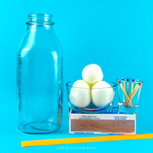 6th Grade Science Egg Bottle Left Brain Craft Brain Glass bottle with bowl holding three eggs, small glass with matches sitting on a box of matches, and a yellow plastic straw, against a blue background
