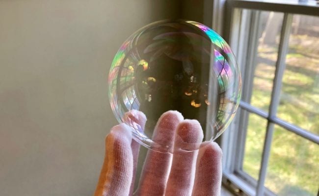 Fourth Grade Science Unpoppable Bubbles Student's gloved hand holding a soap bubble next to a window (Fourth Grade Science)
