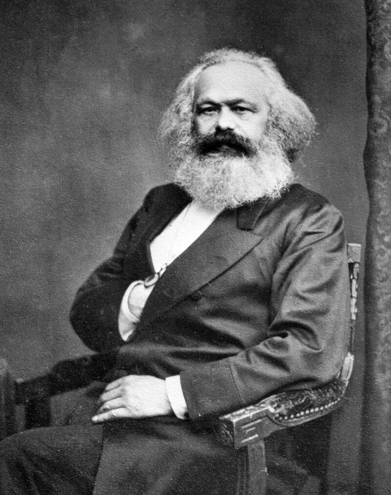 Karl Marx A black and white photograph of a seated man is shown. He has a large beard and his hand is in his suit breast pocket.