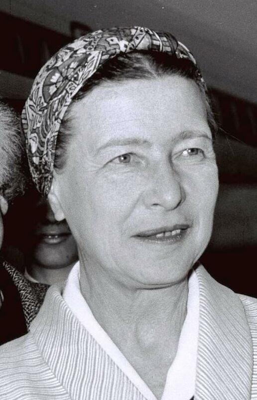 Simone De Beauvoir A middle aged woman is shown in a black and white photograph. Her hair is tied back with a bandana.
