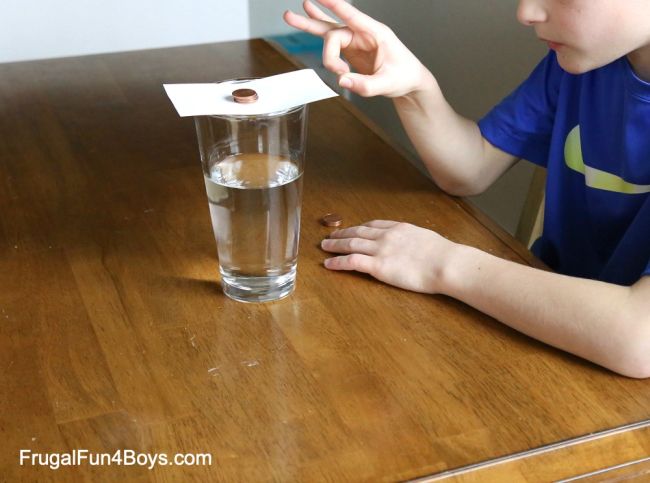 Third Grade Science: Penny Inertia Third grade science student flicking an index card out from underneath a stack of pennies suspended over a cup of water